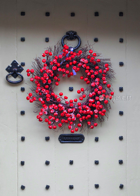 在科茨沃尔德格洛斯特郡的塞伦塞斯特，装饰节日的手工樱桃/浆果花环挂在一扇古老的小屋木板门上。